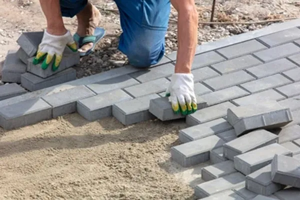 Professional paver repair technician laying brick pavers in herringbone pattern on sand bed